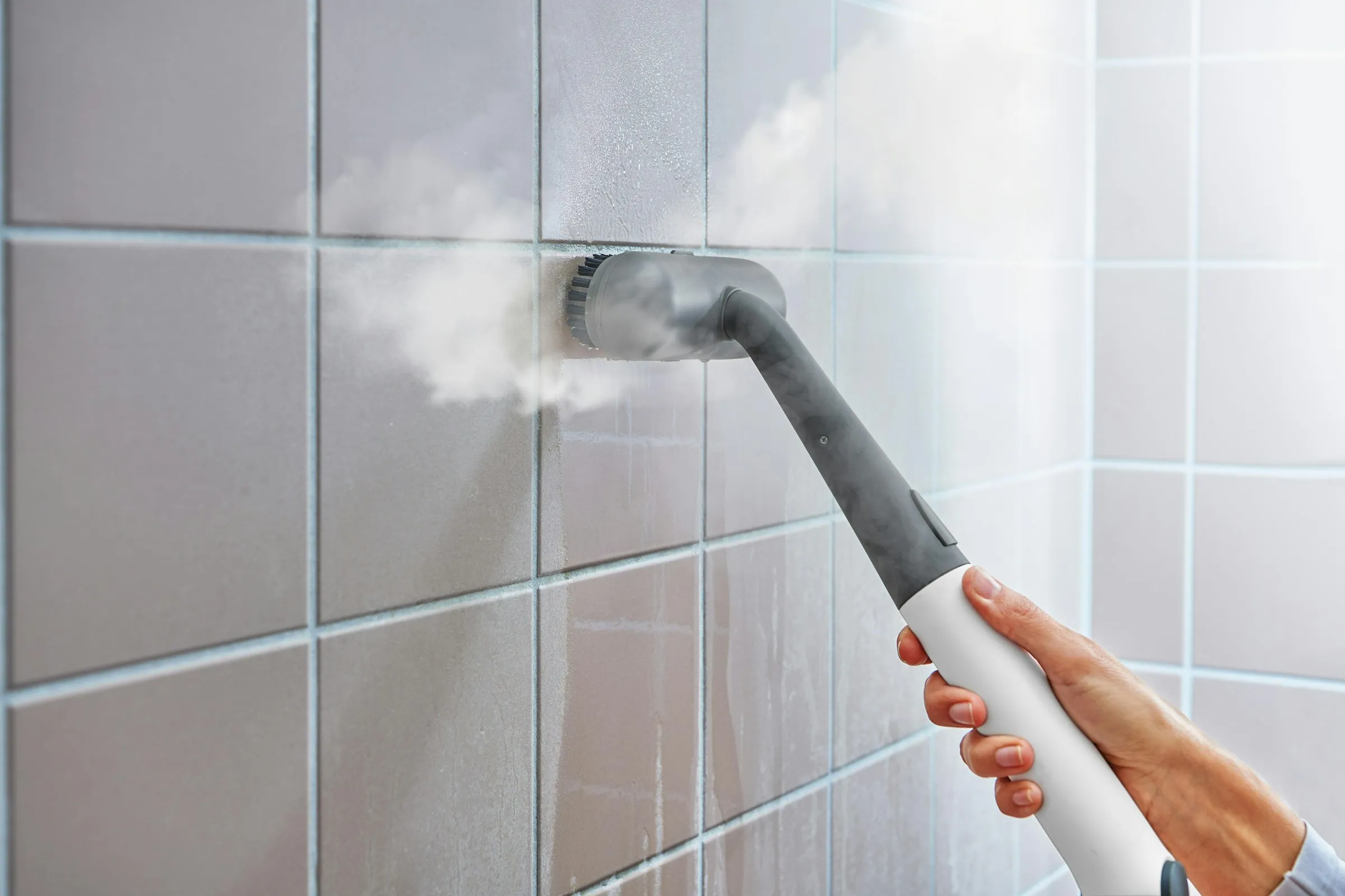 A steam cleaner being used on the tiled wall of a bathroom