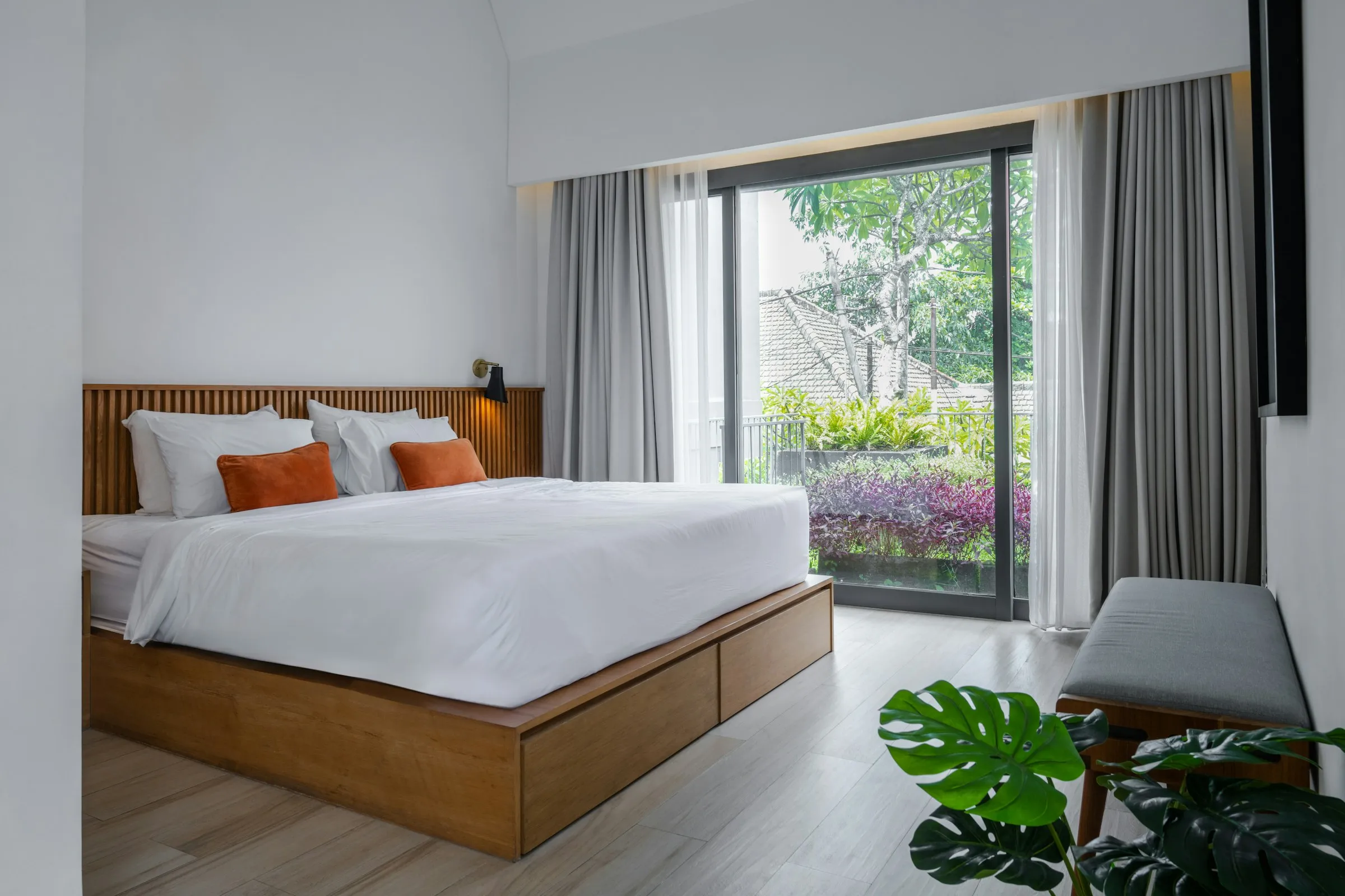 A bright villa bedroom with a freshly made white bed and a sliding door onto a garden